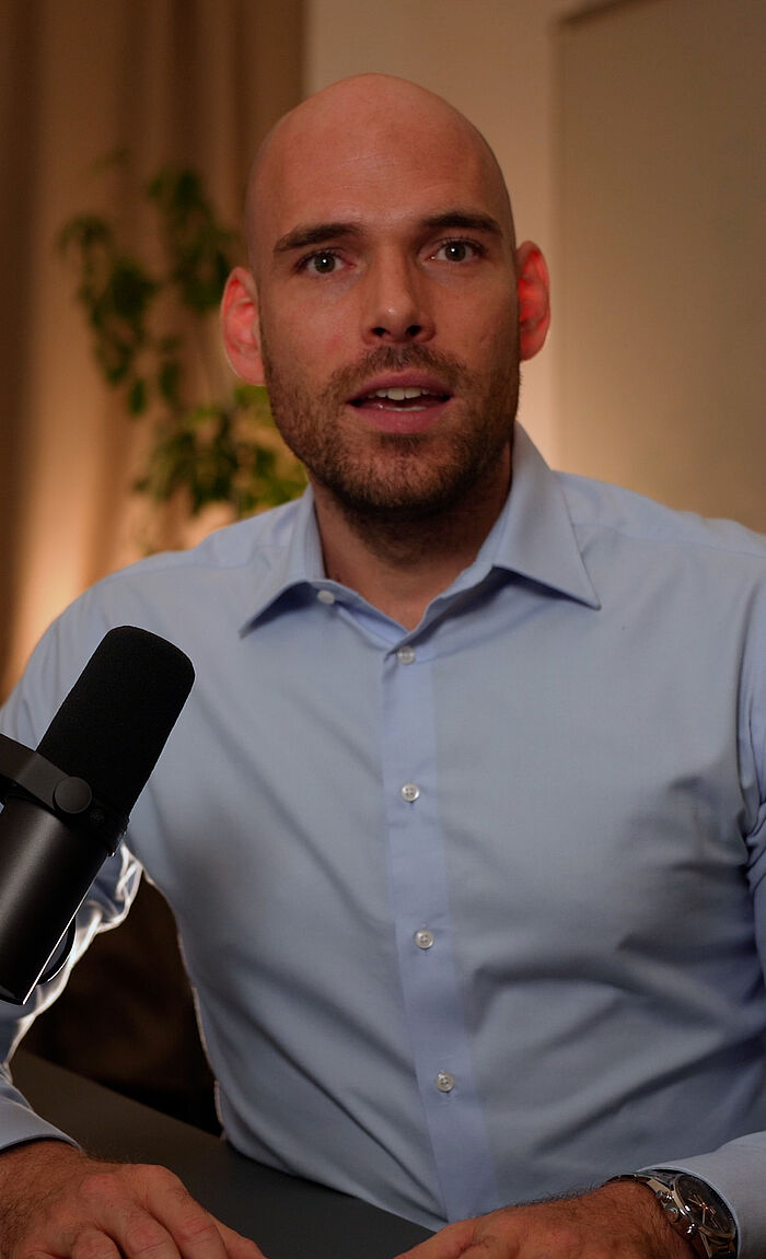 Michael Feer mit einem hellblauen Hemd und ins Mikrophon sprechend